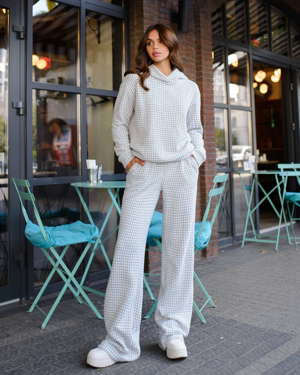 Woman in a checkered outfit standing outside a cafe.