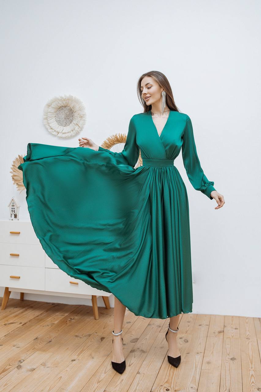 Woman in a green dress posing in a room with wooden floor and white wall.