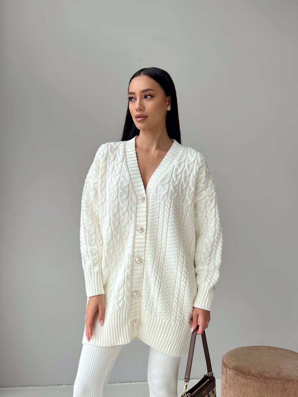 Woman wearing a white cable knit cardigan against a plain background