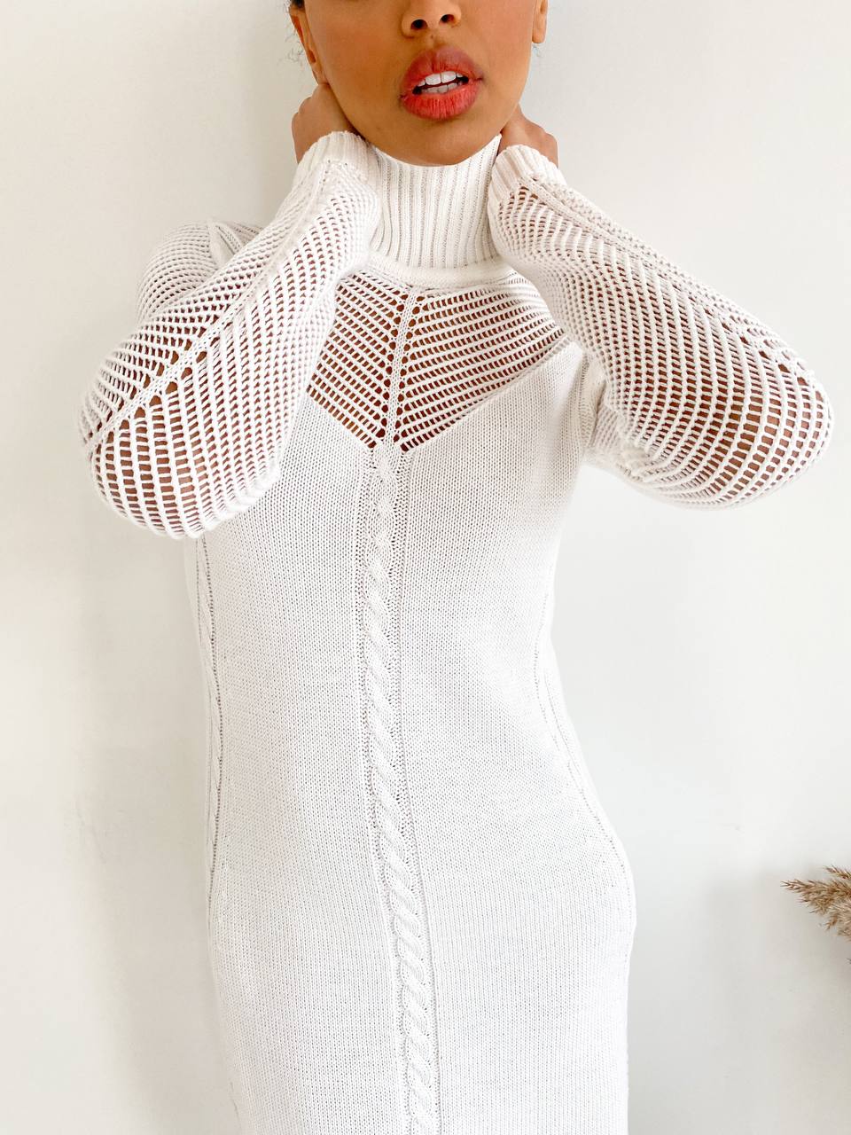 Person wearing a white knit dress with a unique cut-out design on a plain background