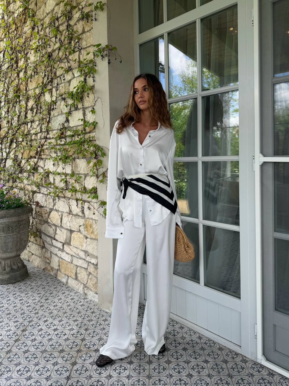 Woman in white outfit standing outside a stone-walled building with glass doors.