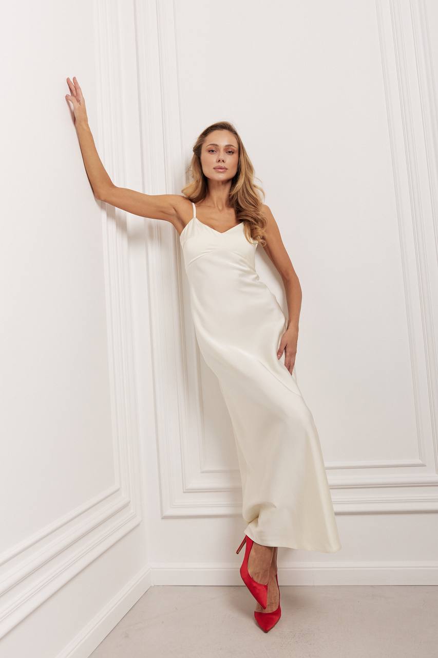 Woman in a white dress with red shoes standing against a white wall.