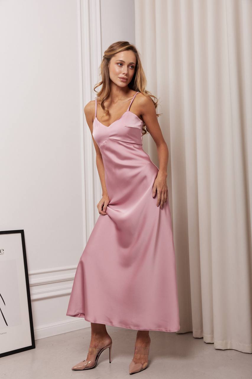 Woman wearing a pink satin dress standing against a white curtain.