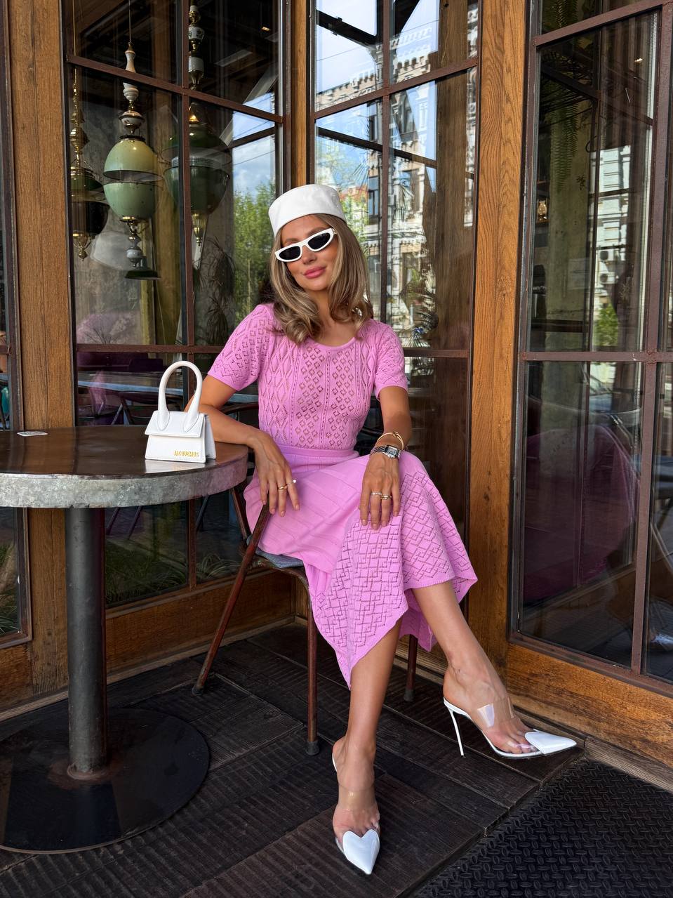 Woman in a pink dress sitting at a table with large windows in the background