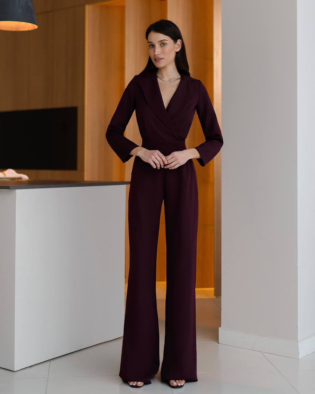 Woman wearing a burgundy jumpsuit standing in an indoor setting.