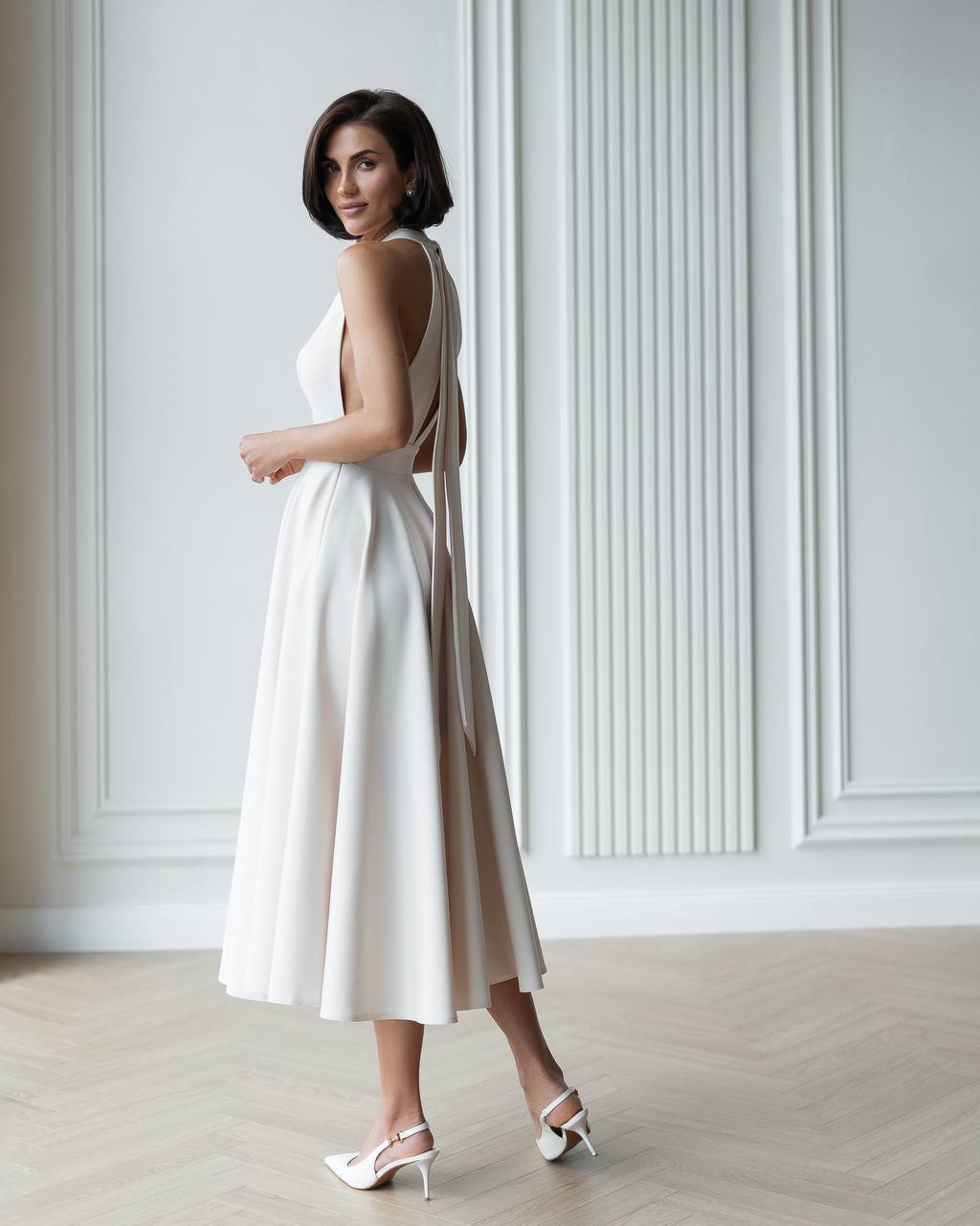Woman wearing a white dress with a backless design in a minimalistic setting.