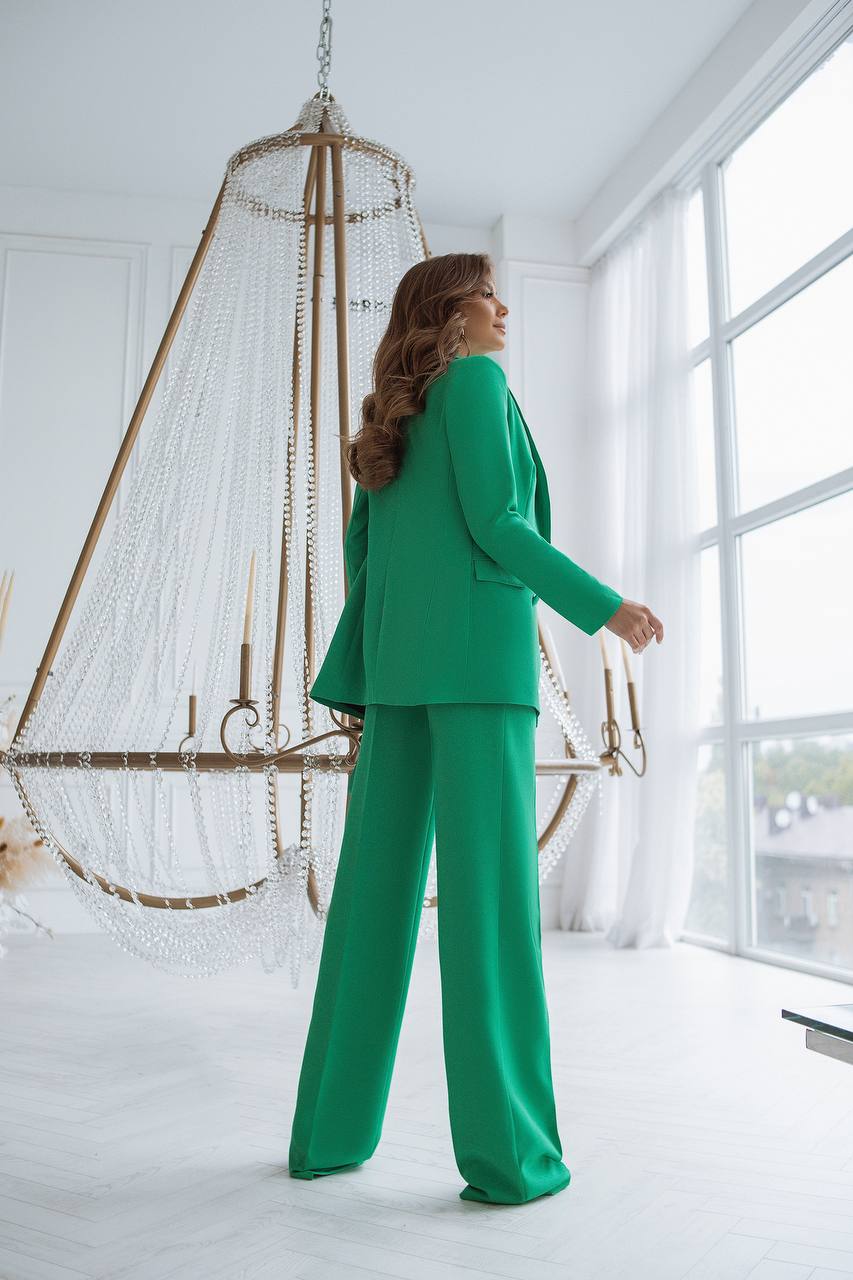 Woman in a green suit standing in a bright room with large windows.