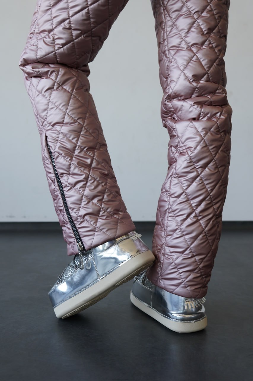 Quilted brown pants with silver high-top sneakers on a dark floor.