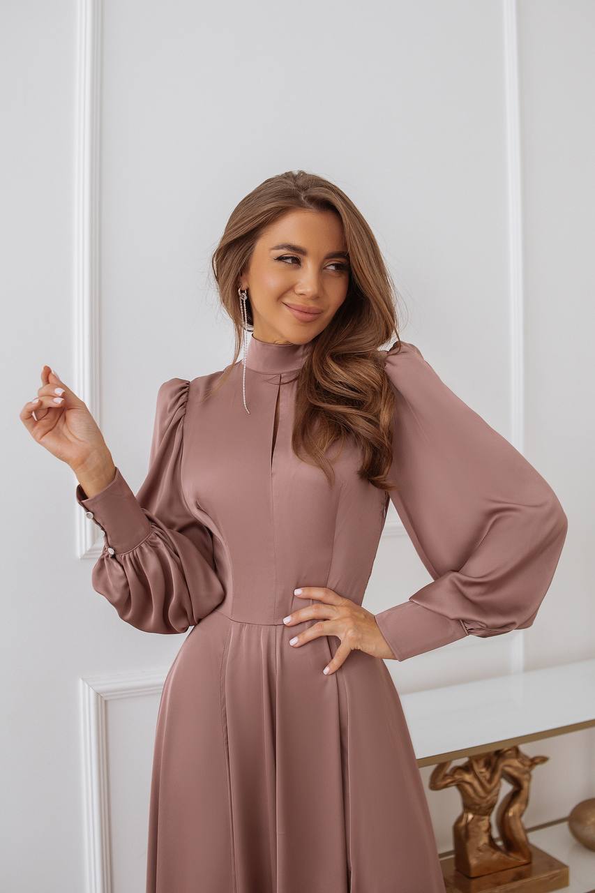 Woman wearing a pink dress with long sleeves against a white wall.