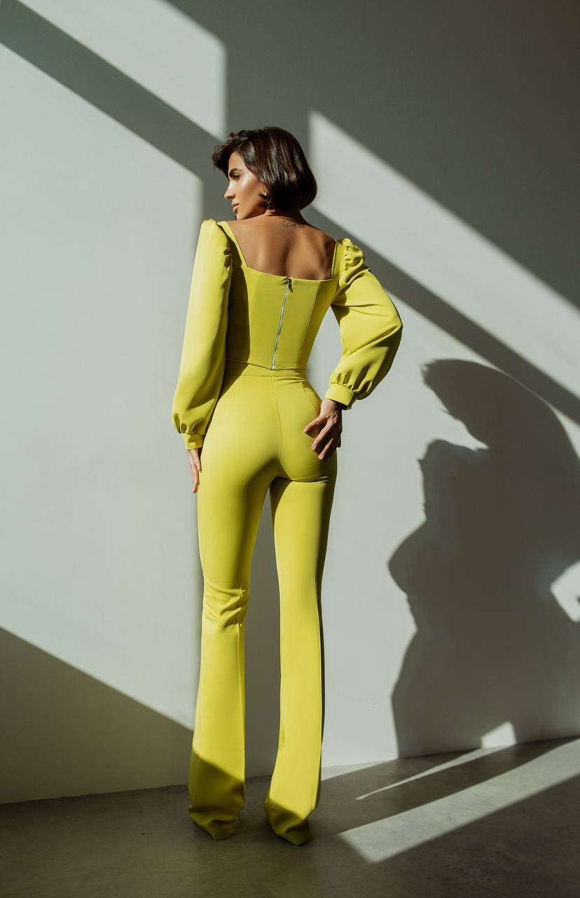 Woman in a bright yellow jumpsuit standing against a wall with light and shadow patterns.