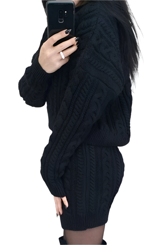 Person wearing a black cable knit sweater taking a mirror selfie.