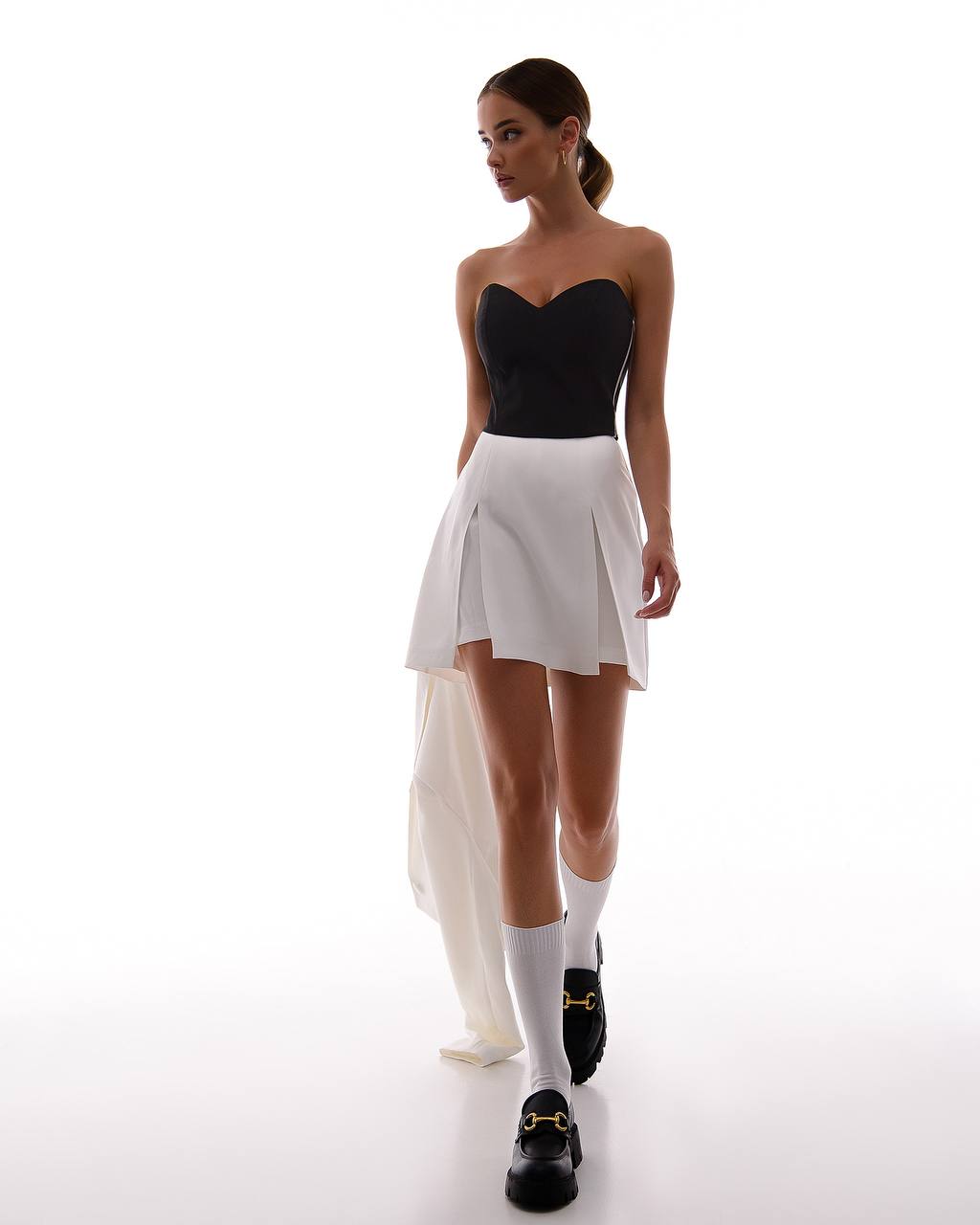Woman wearing a black strapless top and white pleated skirt on a white background