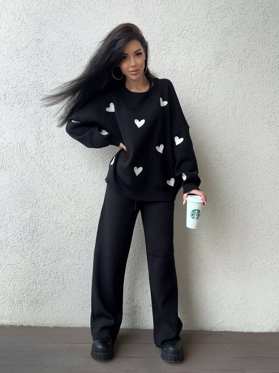 Person wearing a black sweater with white heart patterns against a plain background