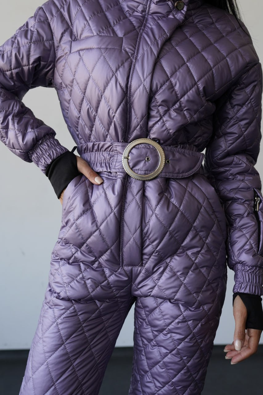 Person wearing a purple quilted jumpsuit with a belt against a neutral background