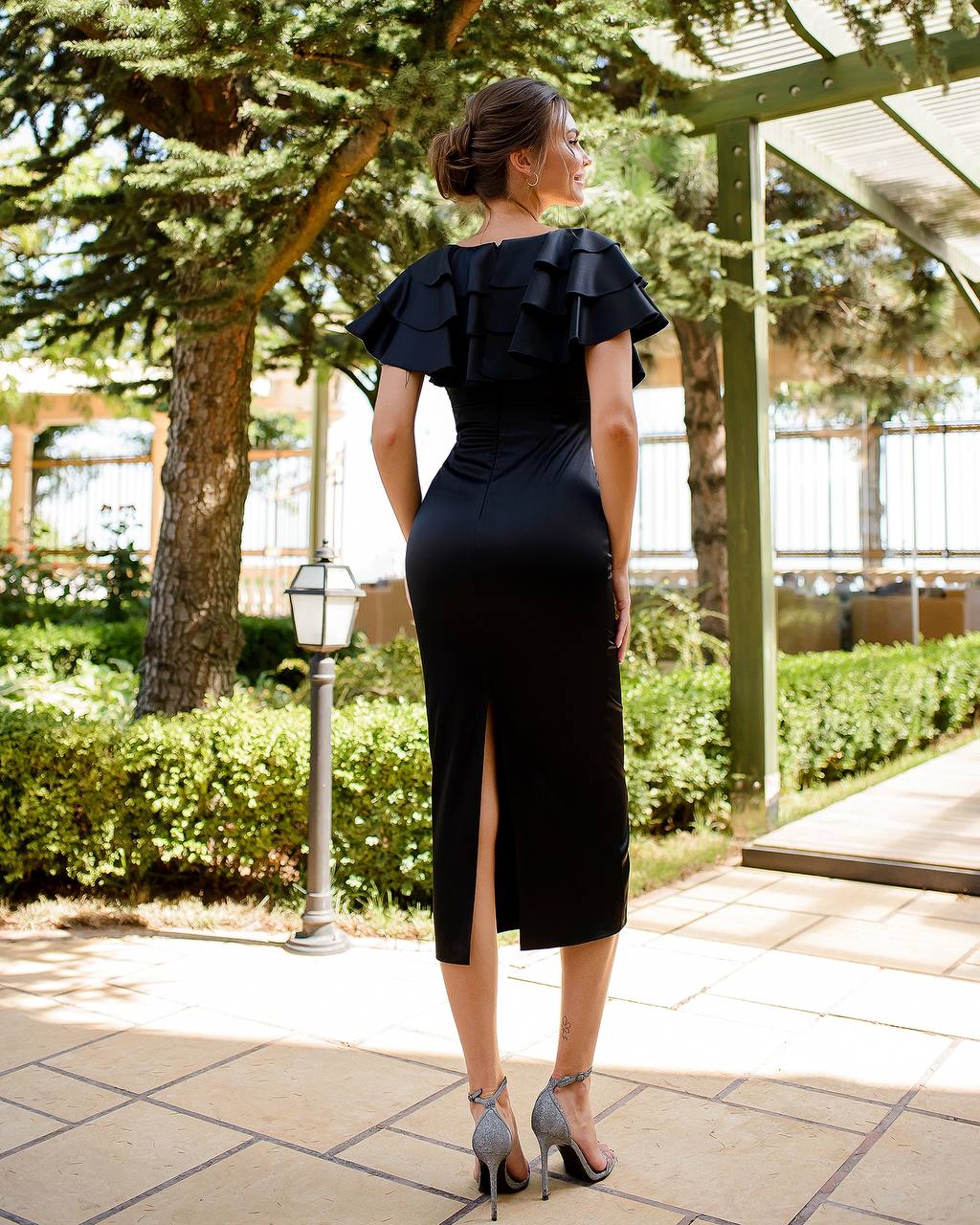 Woman in a black dress with ruffled shoulders standing outdoors on a sunny day.