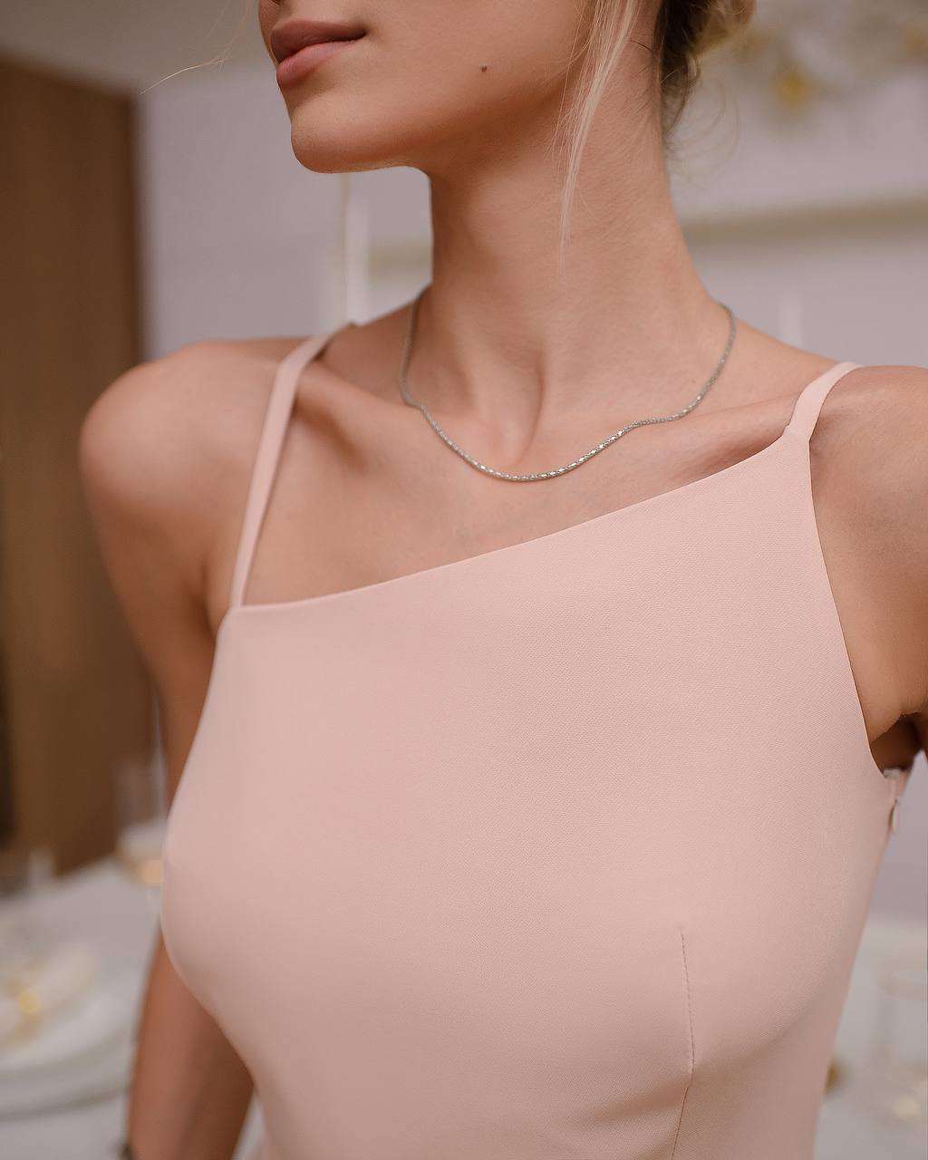 Woman wearing a light pink dress with thin straps and a delicate necklace.