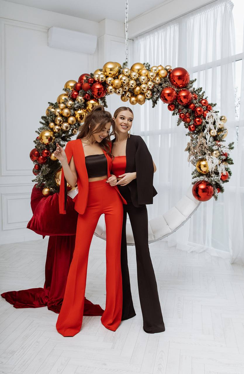 Two women posing in front of a decorative Christmas wreath with red and gold ornaments.