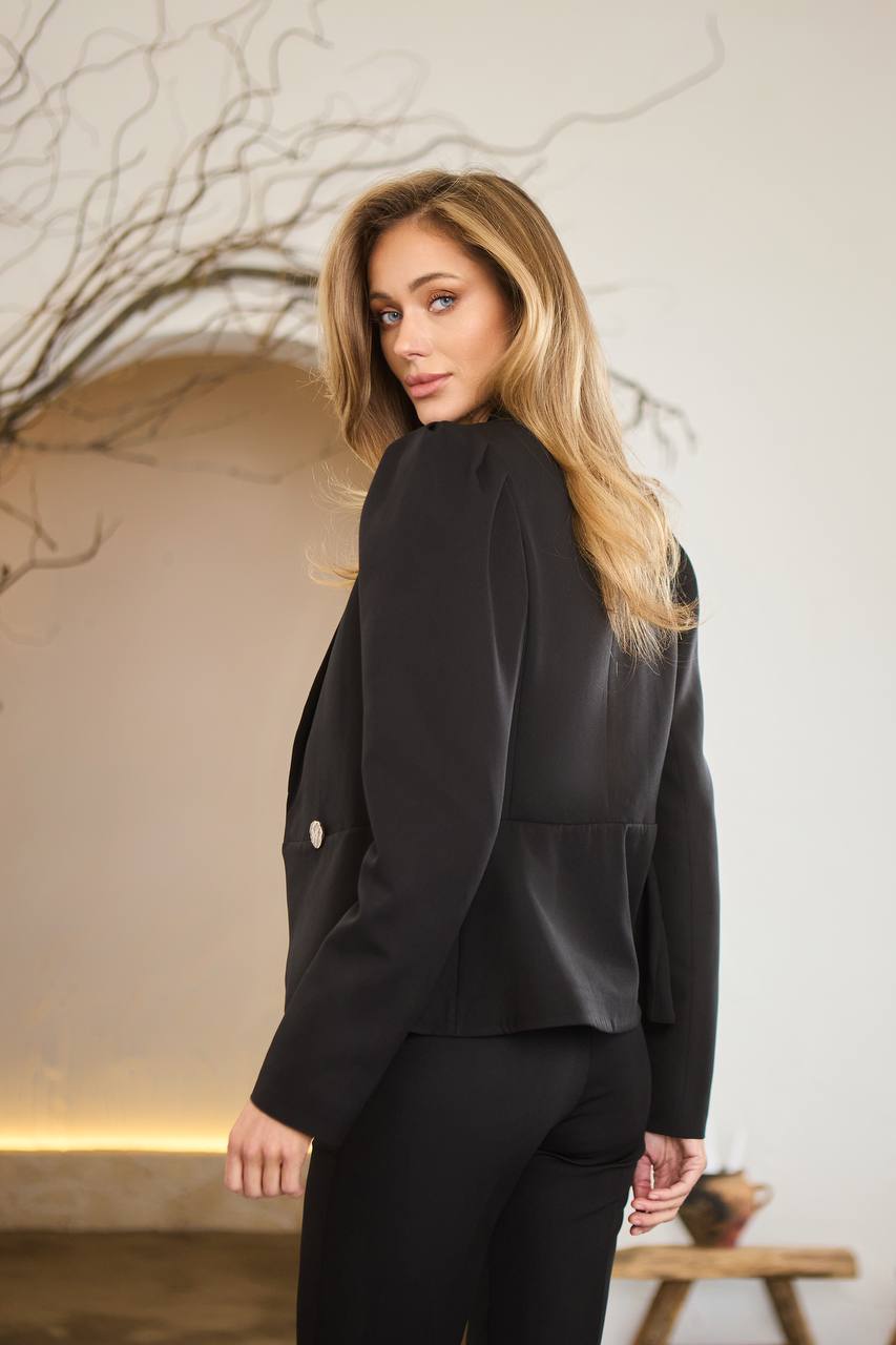 Woman wearing a black suit standing in a room with a neutral background