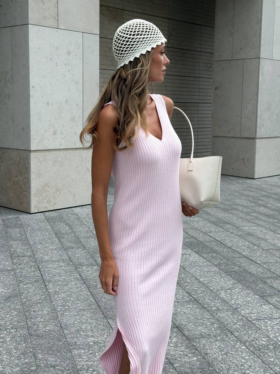 Woman in a pink dress and white knit cap walking outdoors on a city street.