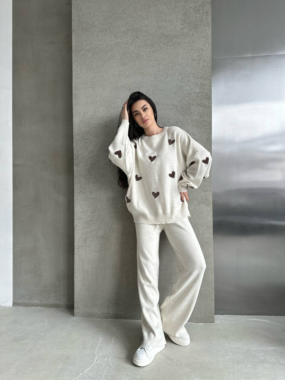 Woman wearing a white outfit with heart patterns against a gray wall.