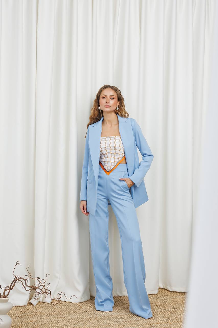 Woman in a light blue suit standing against a white curtain