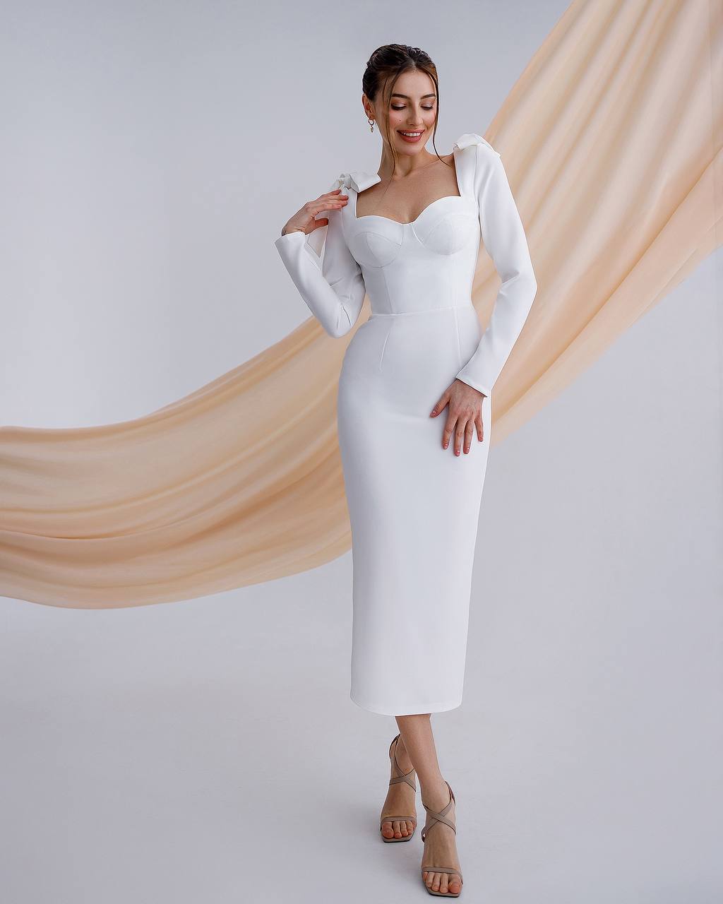 Woman wearing a white dress with a matching cardigan against a draped fabric background