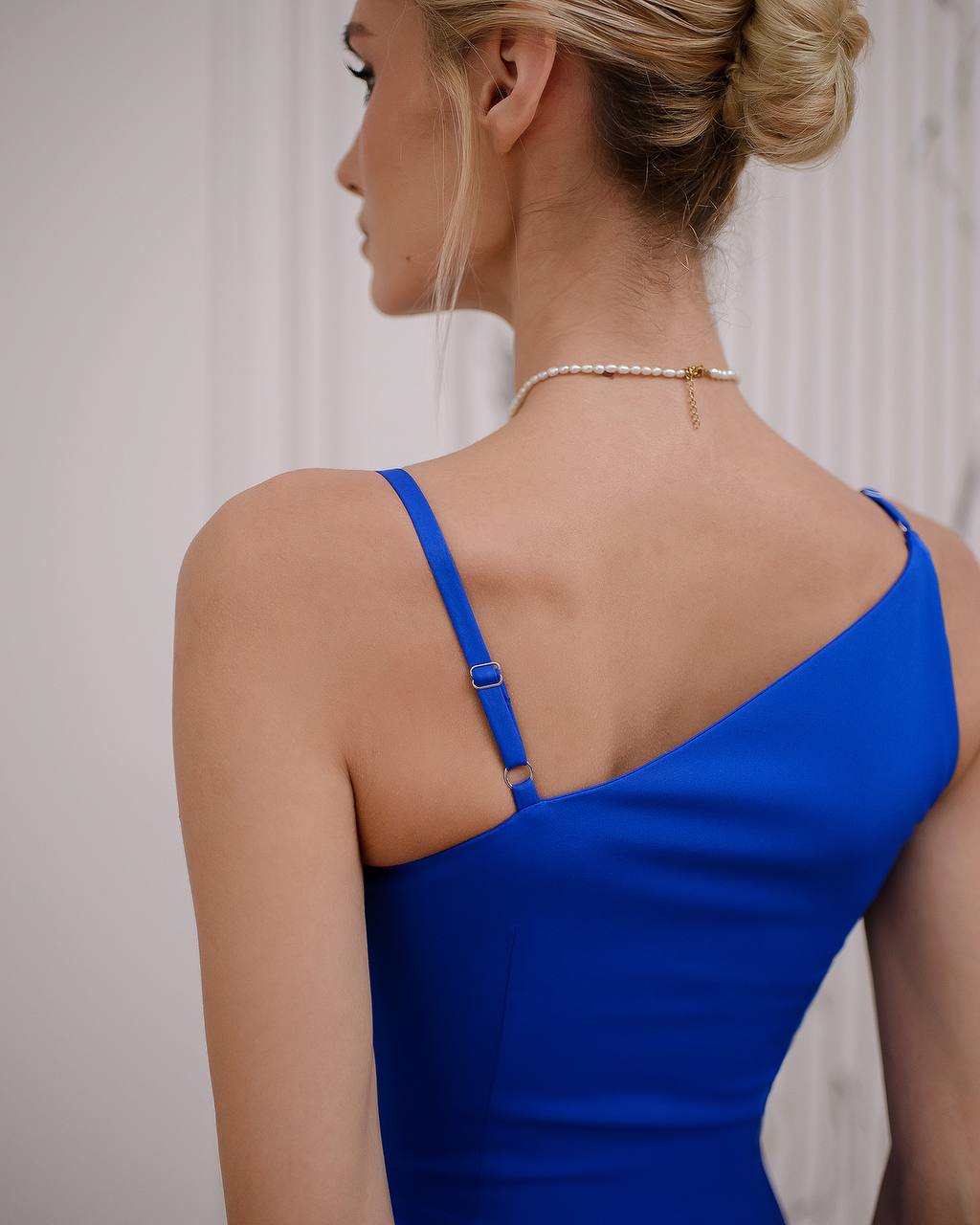 Woman wearing a blue dress with thin straps, back view.