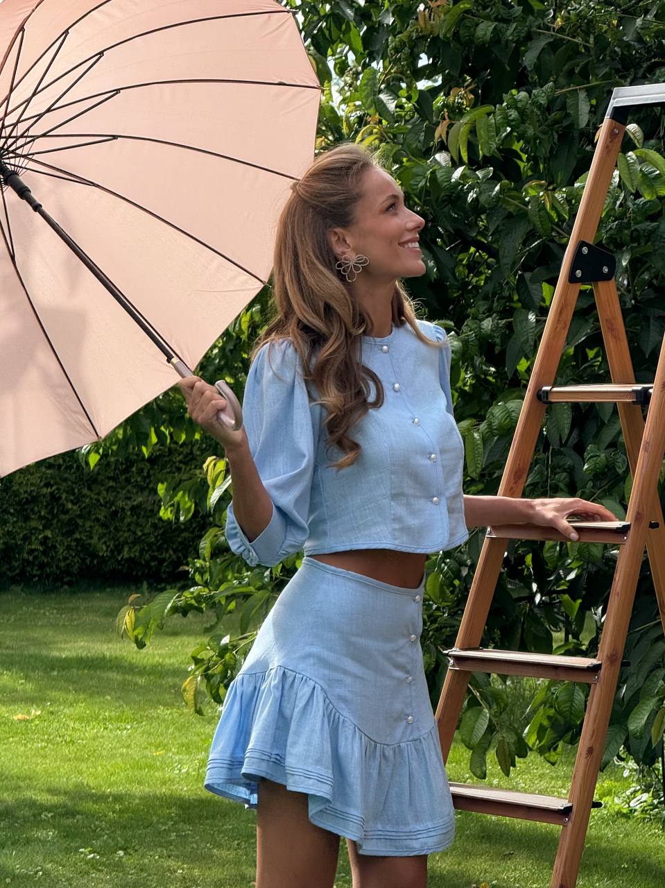 Woman in a light blue outfit holding an umbrella in a garden setting