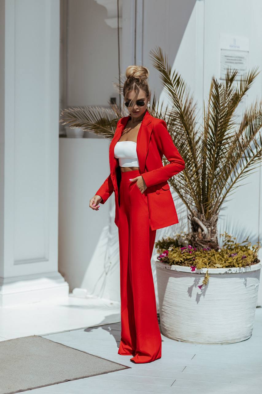 Woman in a red suit standing in a modern indoor setting with plants.