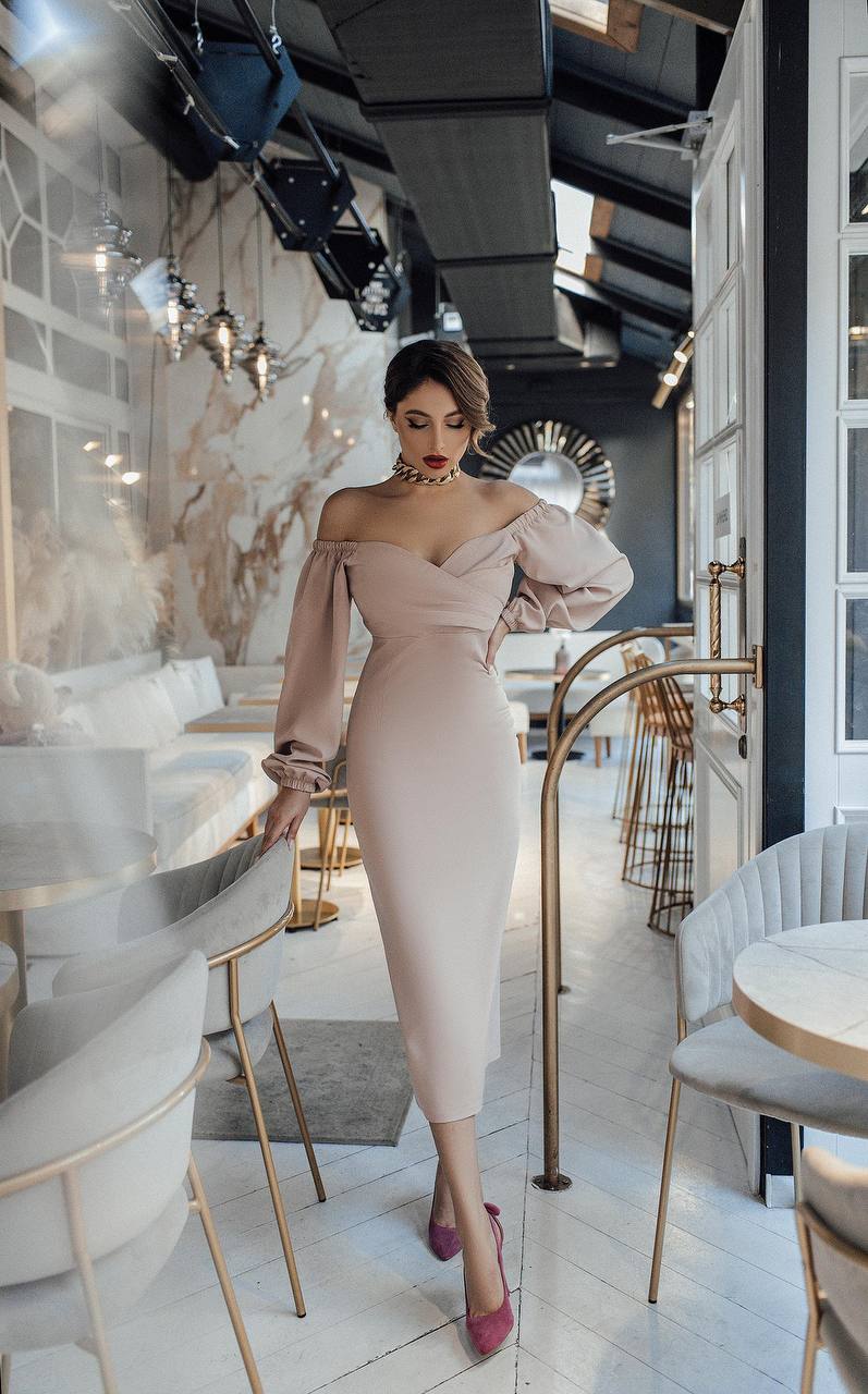 Woman in a stylish off-shoulder dress standing in an elegant interior setting.