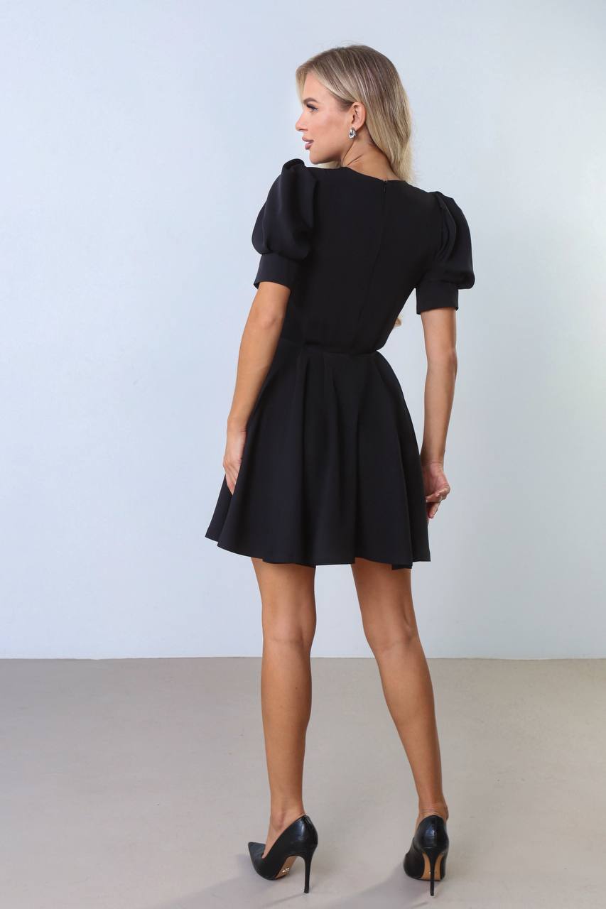 Woman wearing a black dress with puffed sleeves against a white background