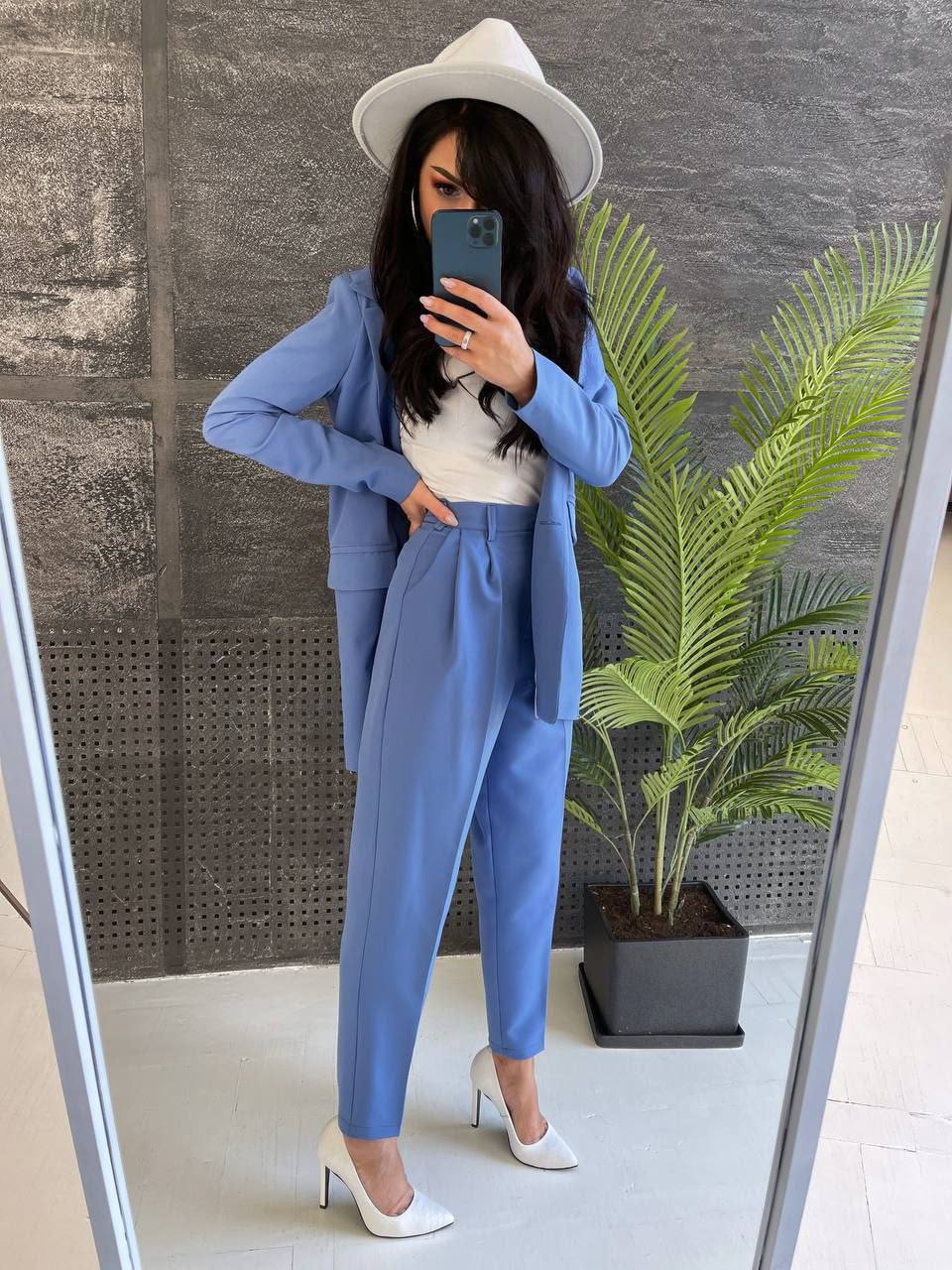 Woman in a blue suit and white hat taking a mirror selfie.