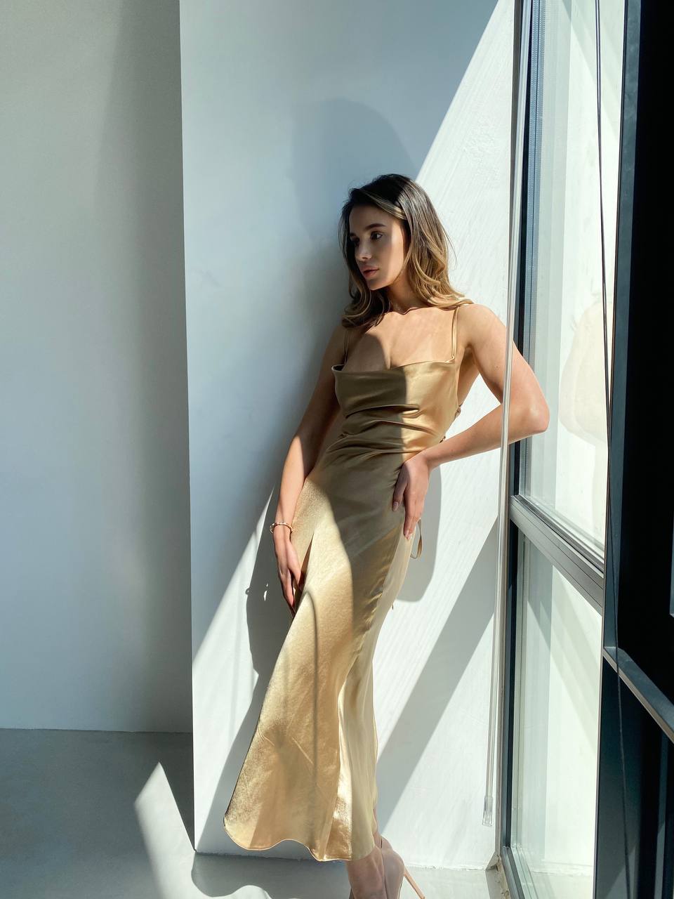 Woman in a gold dress standing by a window in a modern interior.