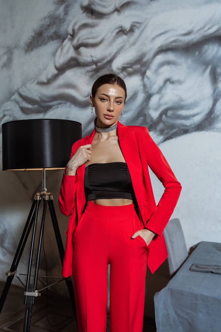 Woman in a red outfit standing in front of a textured wall with a lamp and suitcase.