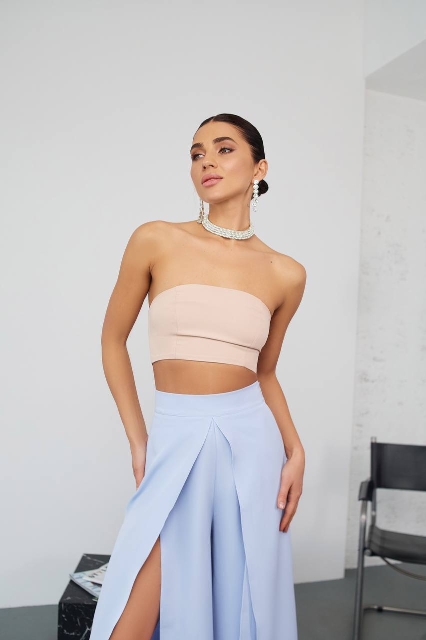 Woman wearing a beige strapless top and light blue skirt with a white background