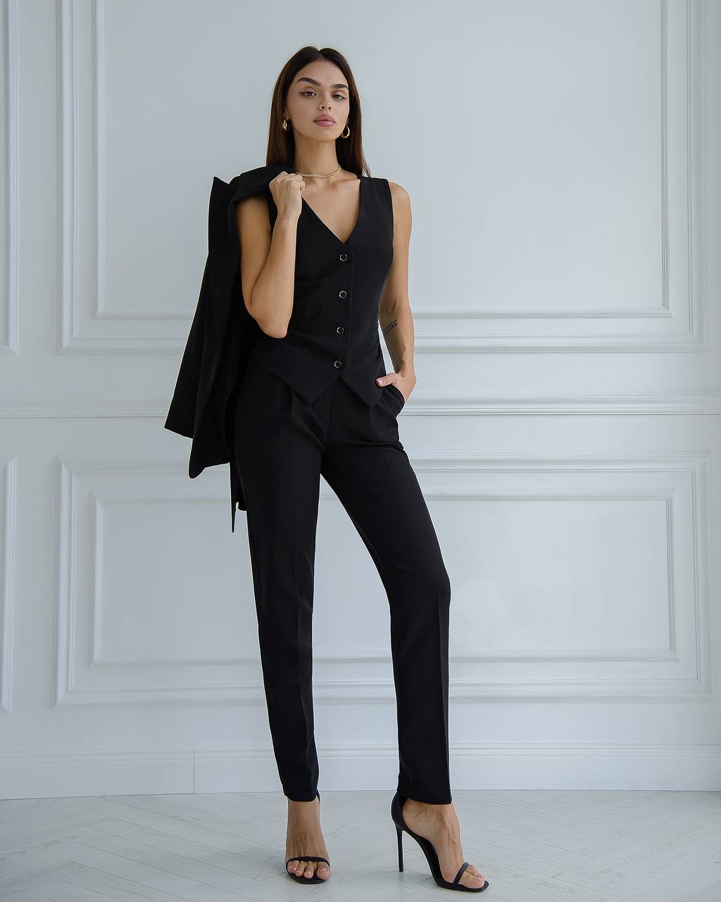 Woman wearing a black suit against a white paneled wall