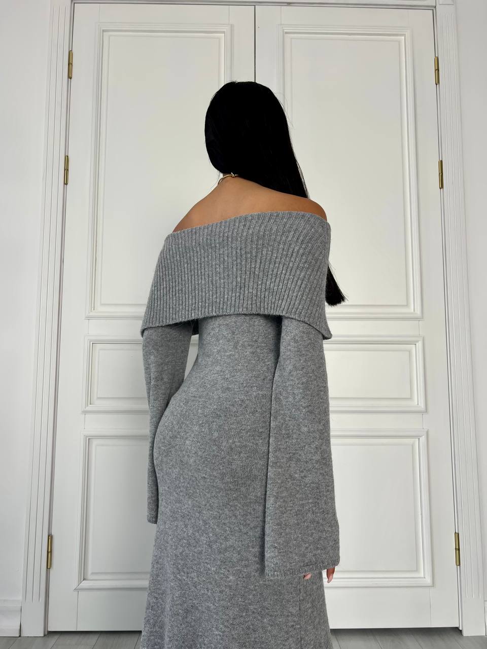 Person wearing a gray off-shoulder dress standing in front of white paneled doors.