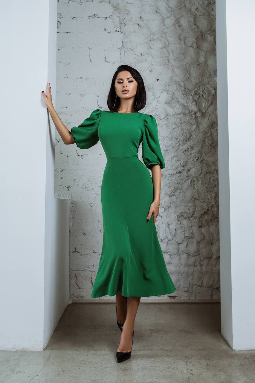 Woman in a green dress standing against a textured wall.