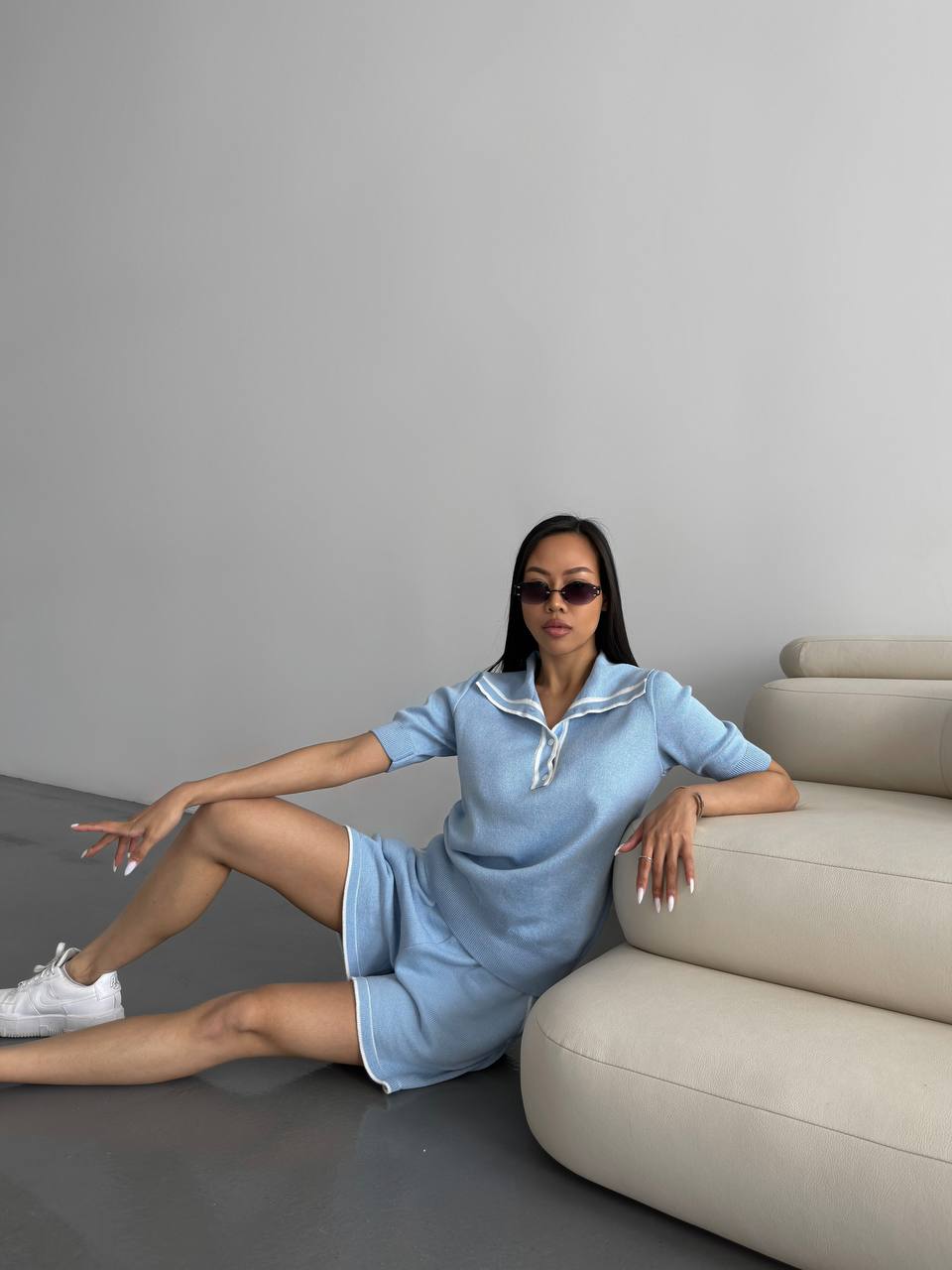 Woman in a light blue dress sitting on a beige sofa against a gray wall.
