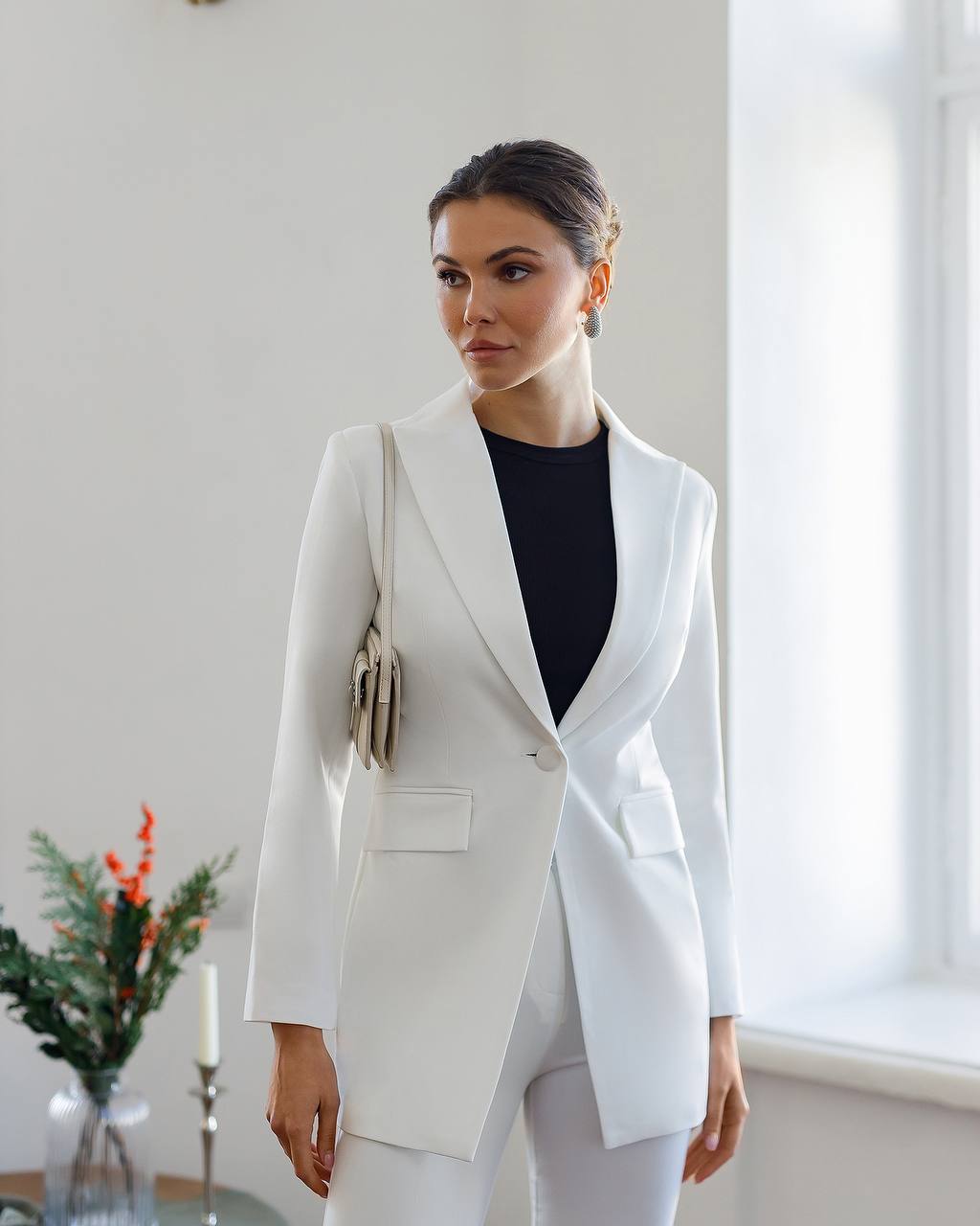 Woman wearing a white blazer and black top in a room with a window and plant.