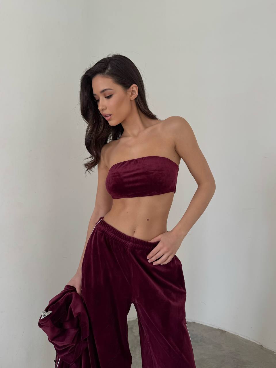 Woman wearing a burgundy strapless top and wide-leg pants against a plain background