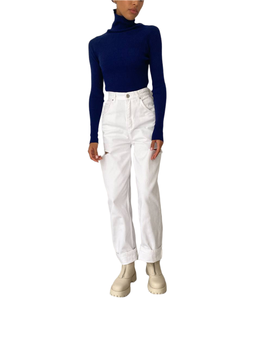 Person wearing a navy turtleneck and white pants on a white background