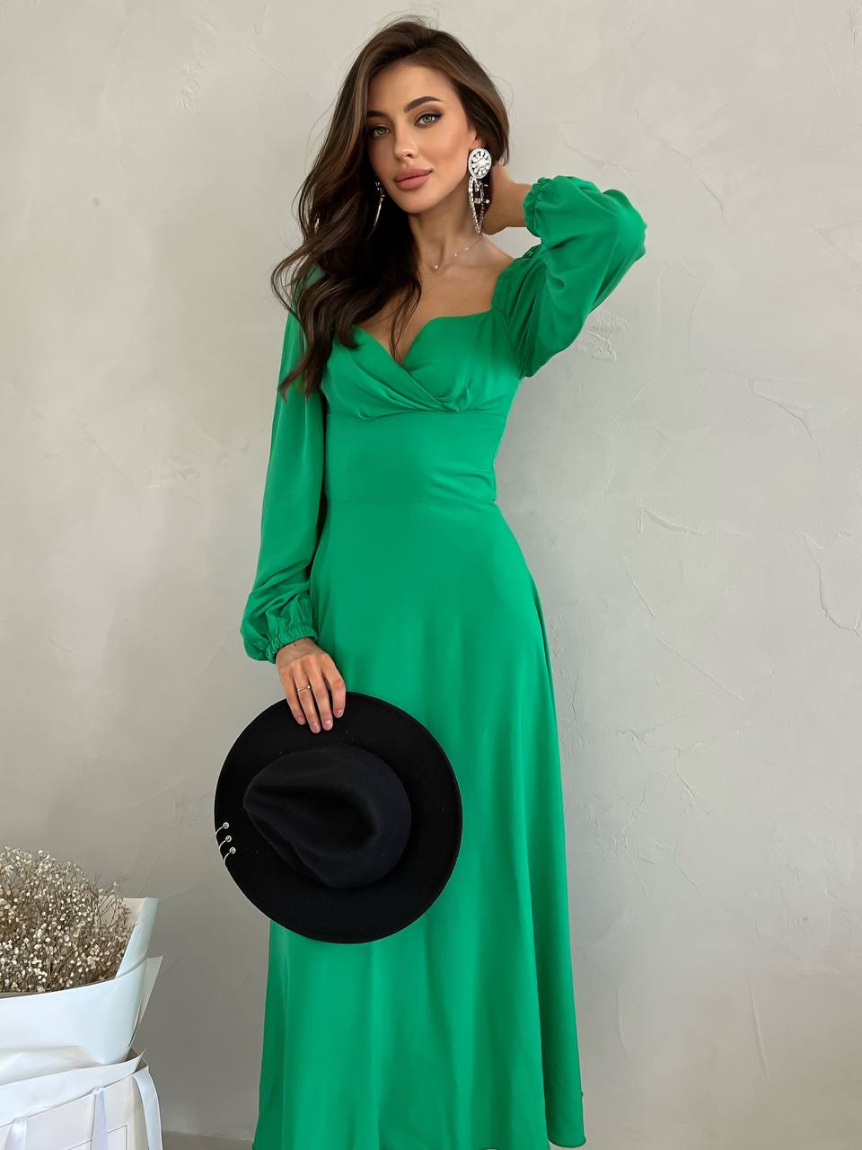 Woman in a green dress holding a black hat against a plain background