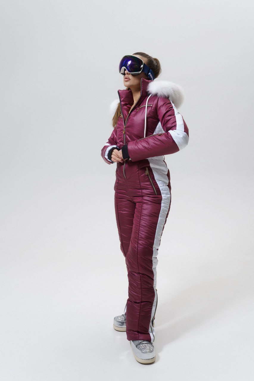 Person wearing a pink and white ski suit with goggles on a white background