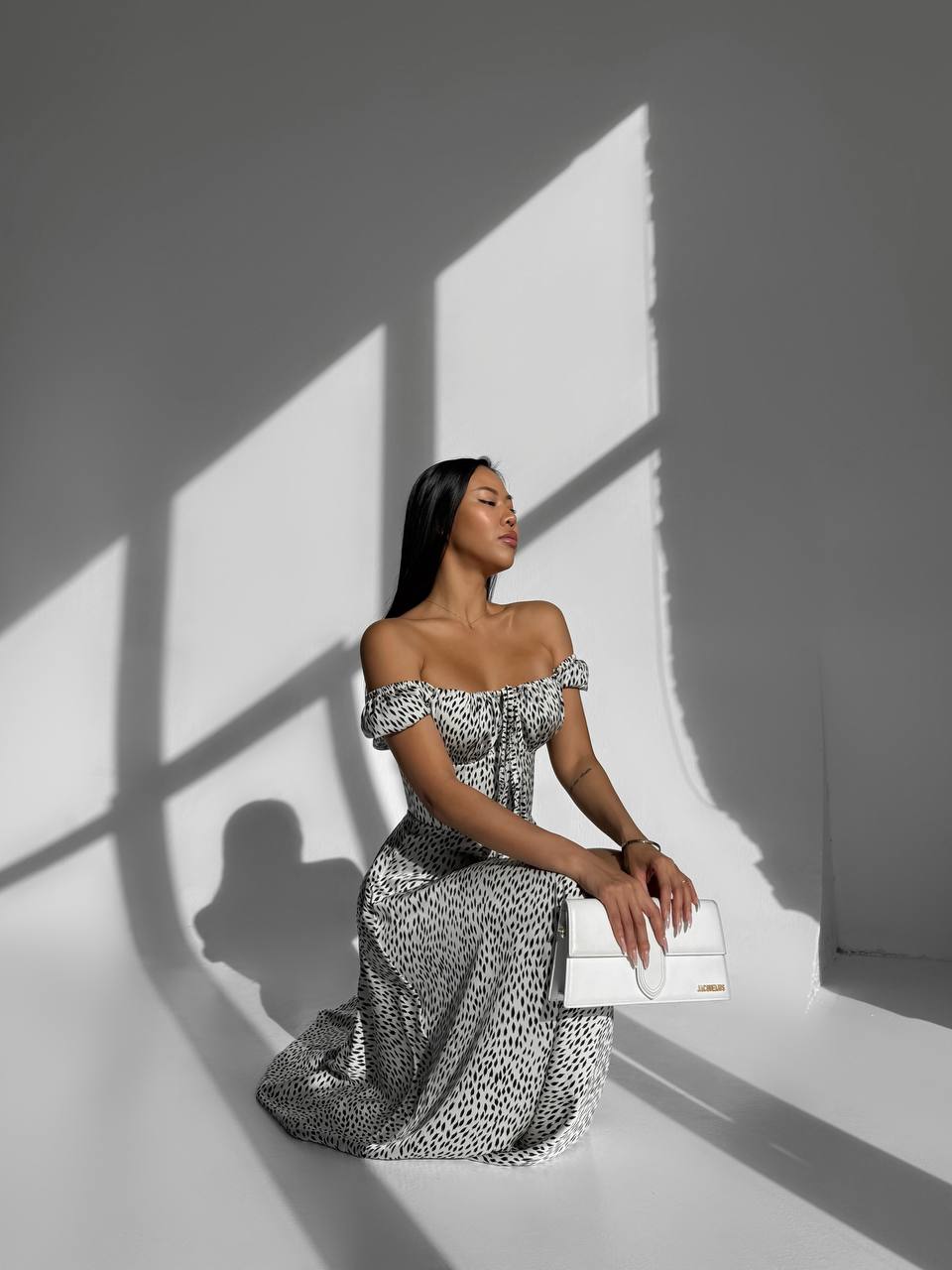 Woman in a patterned off-shoulder dress holding a white clutch against a light background