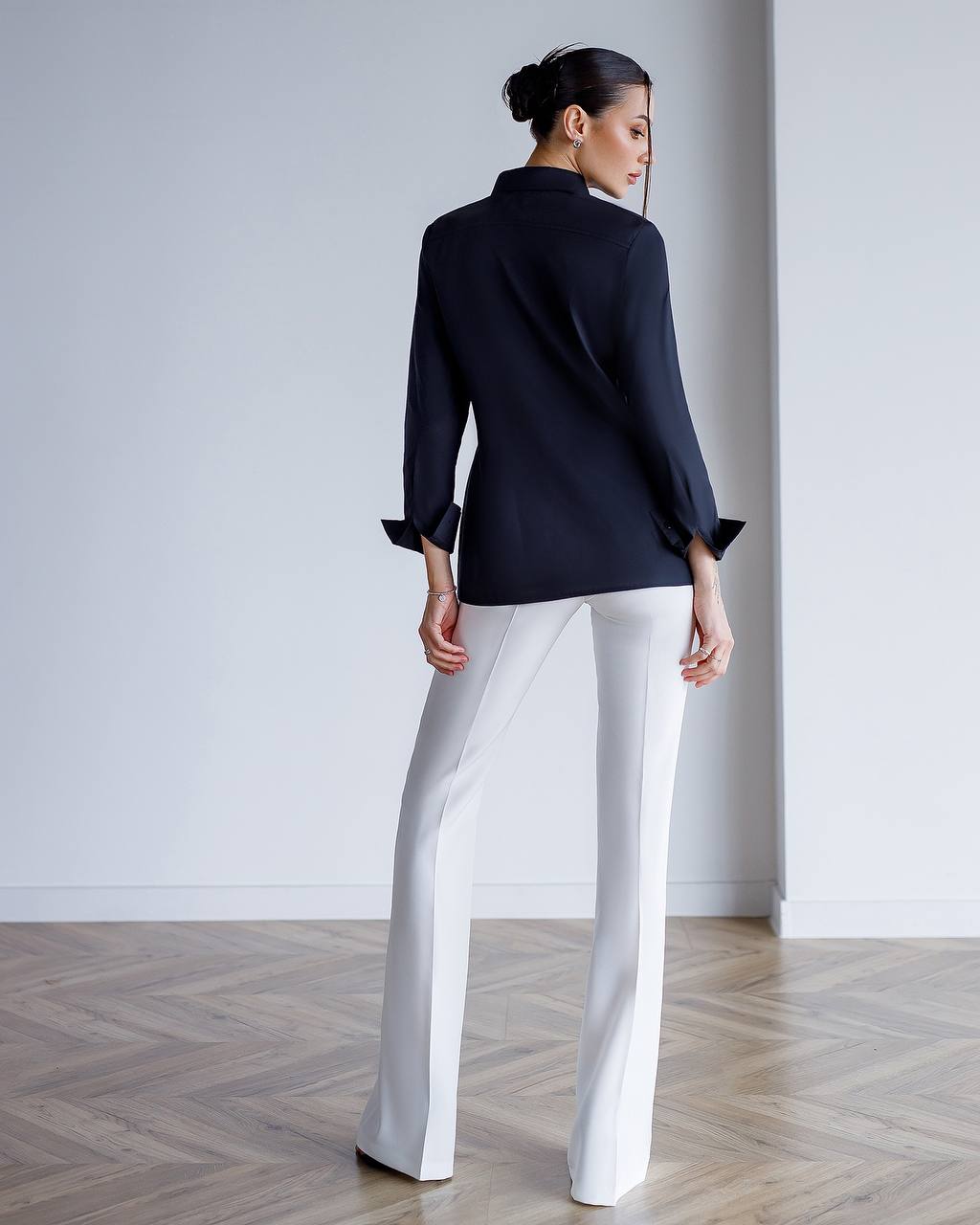 Woman wearing a black blazer and white pants in a minimalistic setting