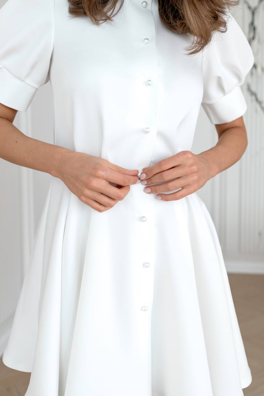 White dress with short sleeves and a button-up front, worn by a person.