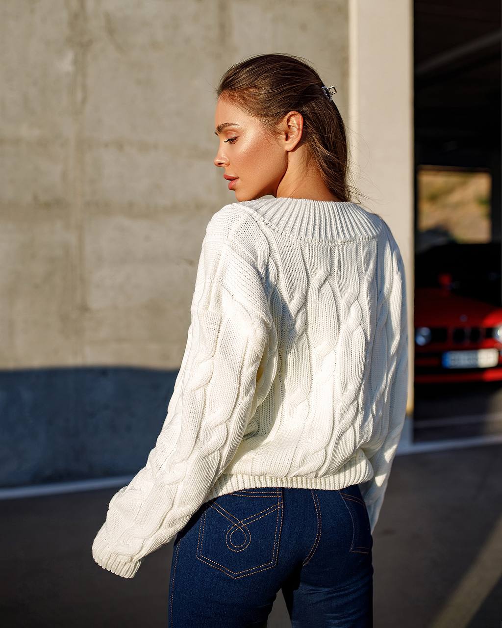 Person wearing a white cable knit sweater and blue jeans standing outdoors.