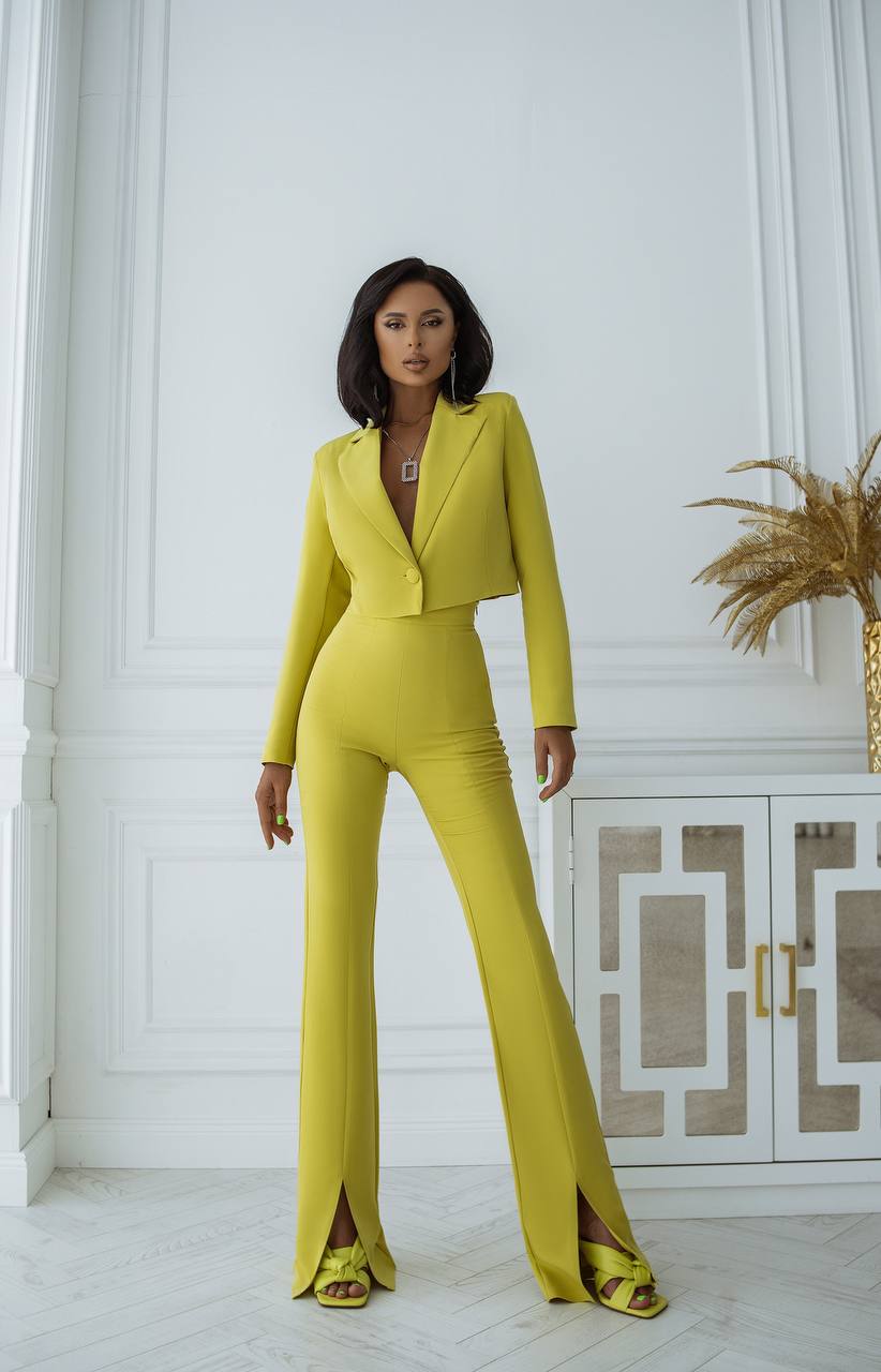 Woman wearing a bright yellow suit in an elegant room with decorative elements.