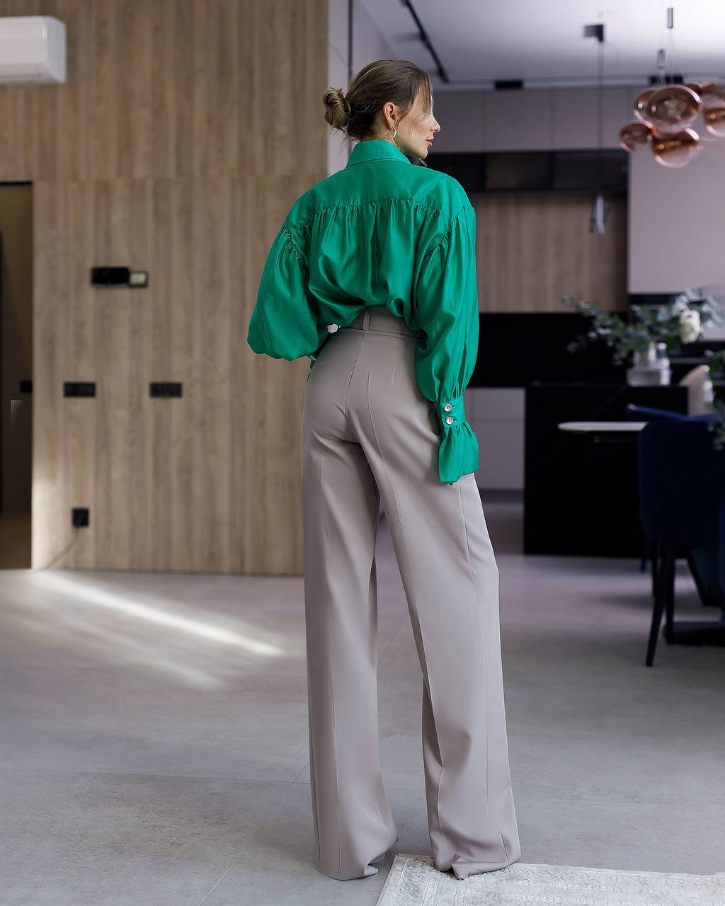 Person wearing a green blouse and beige pants in a modern kitchen.